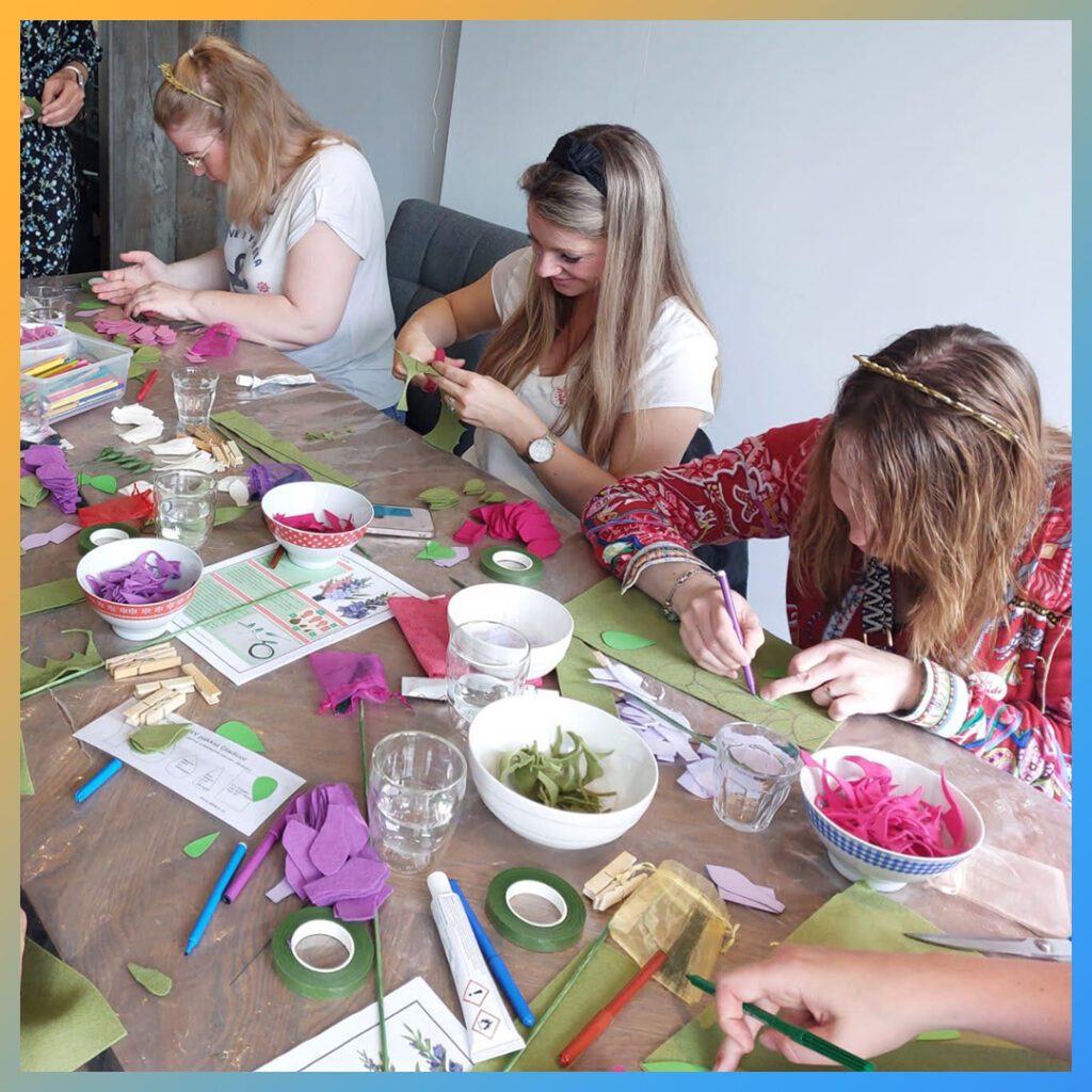 Groep vrouwen maakt vilten bloemen tijdens een vrijgezellenfeest.