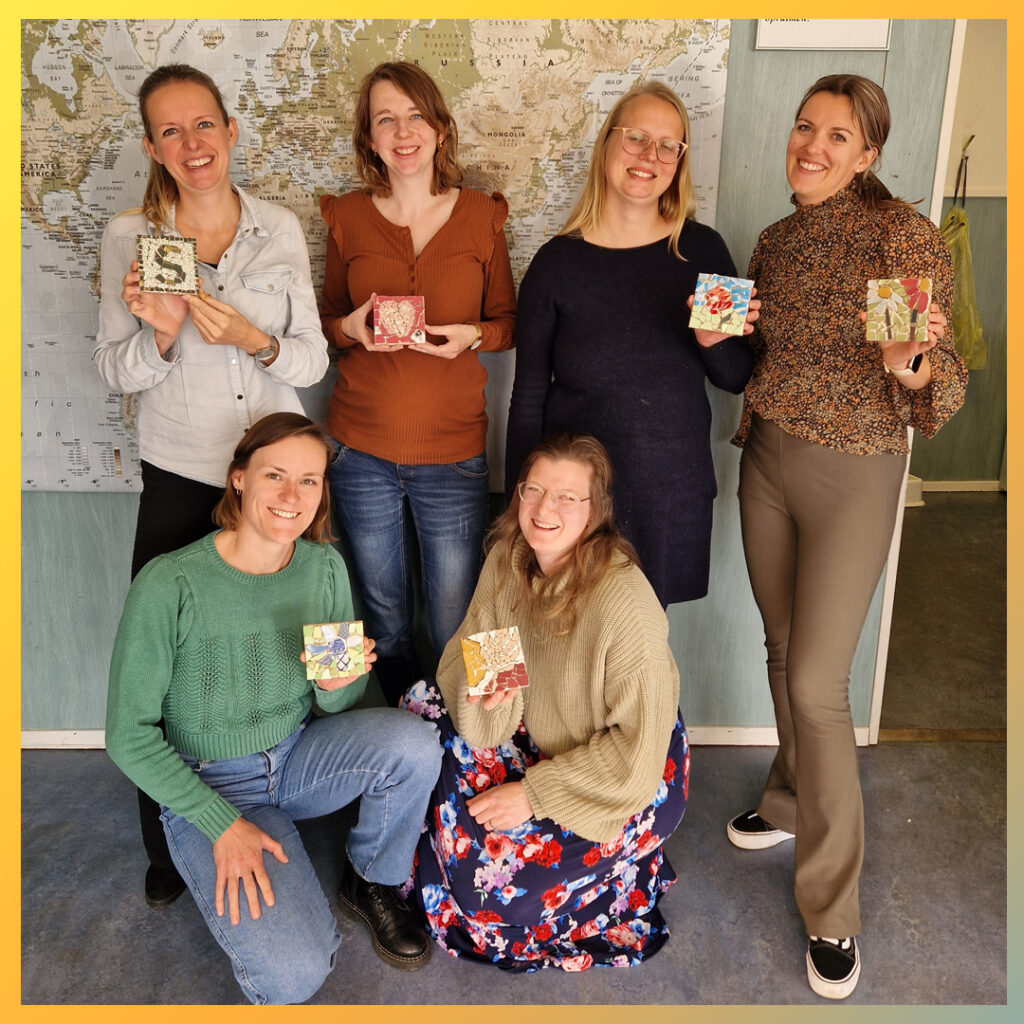 Zes vrouwen tonen trots hun mozaïektegels na afloop workshop.
