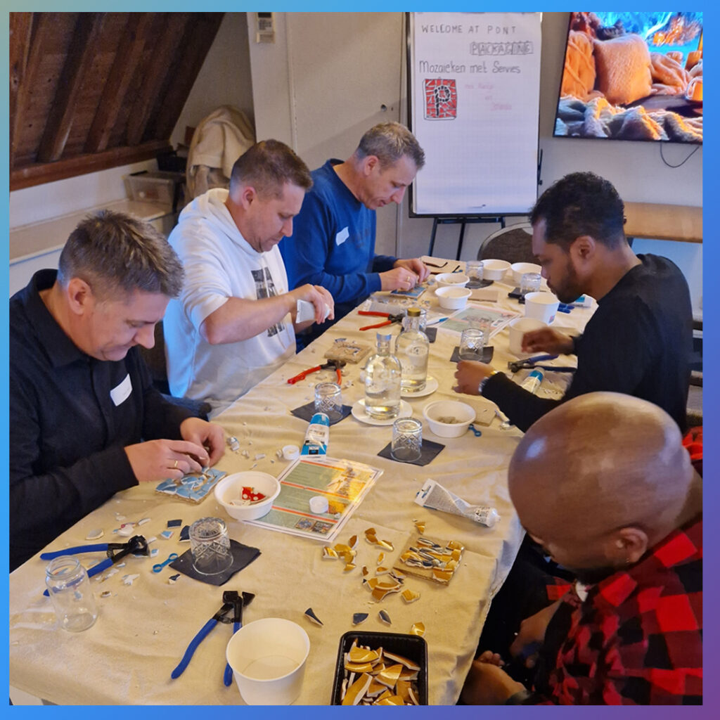 Groep mannen mozaïekt serieus tijdens workshop.