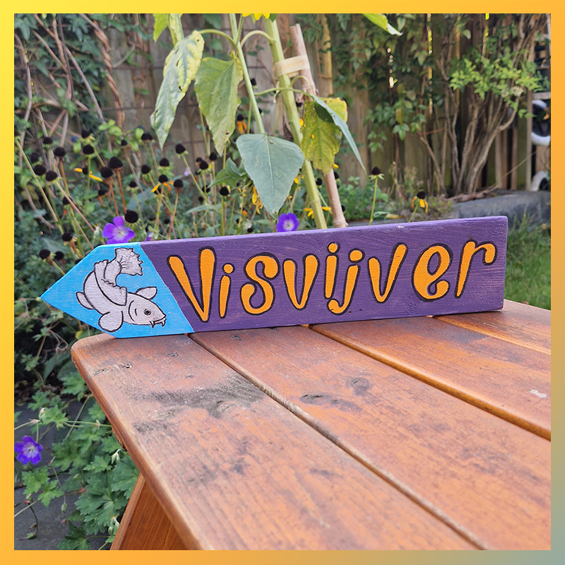 Houten beschilderd wegwijzerbordje met karper dat naar een visvijver wijst