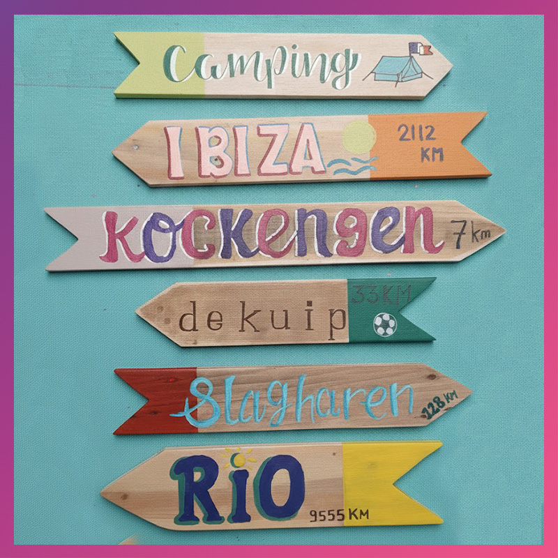 Meerdere houten beschilderde wegwijzerbordjes met plaatsnamen op een groen kleed