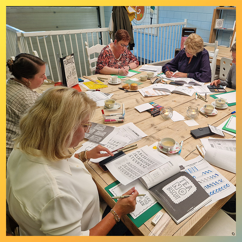 Grote groep vrouwen volgt samen een workshop handlettering aan een lange tafel