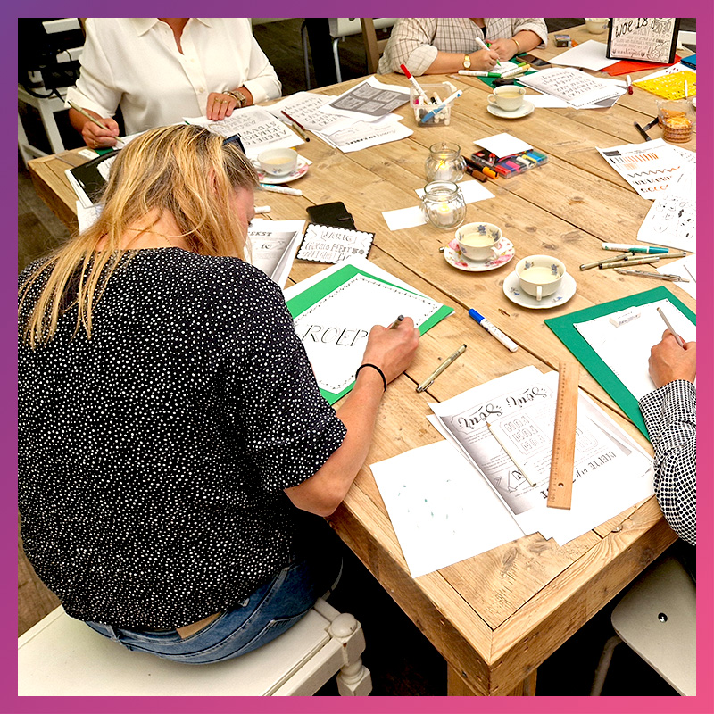 Jonge deelnemer werkt geconcentreerd aan handlettering aan een workshoptafel